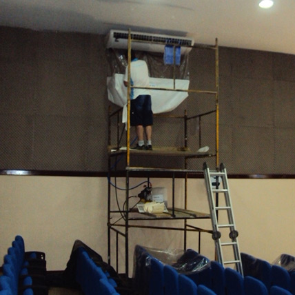 Técnico em andaime realizando limpeza de ar condicionado de grande porte